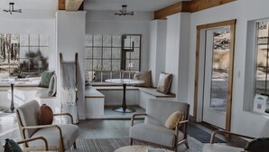 Ein geräumiges Wohnzimmer mit hoher Decke, Holzbalken, Deckenventilator und großen Fenstern mit Blick ins Freie.