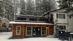 Ein zweistöckiges Holzhaus mit Balkon, umgeben von schneebedeckten Bäumen.
