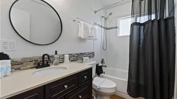 Un baño con espejo redondo, lavabo con grifo, inodoro, bañera con ducha y cortina negra.