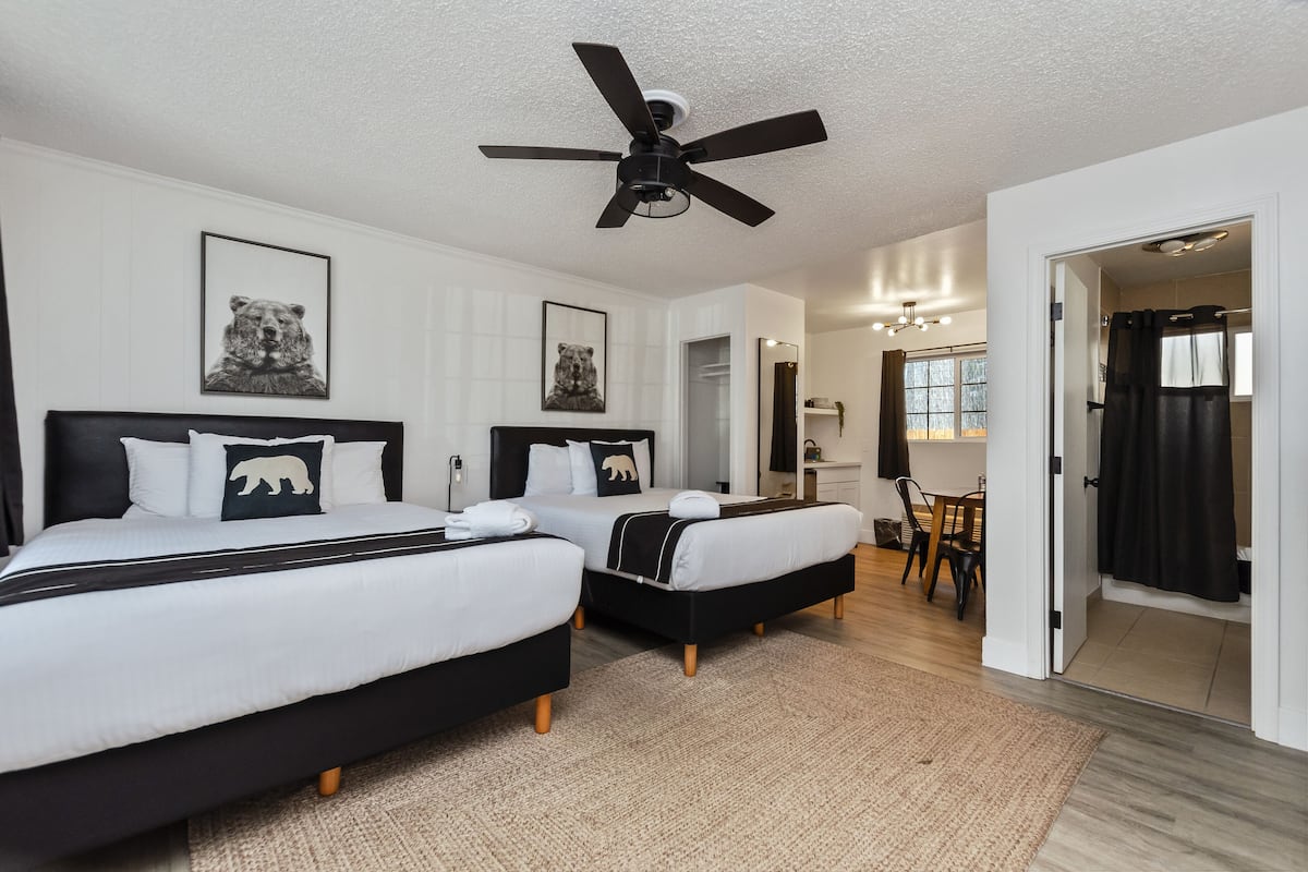 A hotel room with two beds, a ceiling fan, and a dining area visible through an open door.