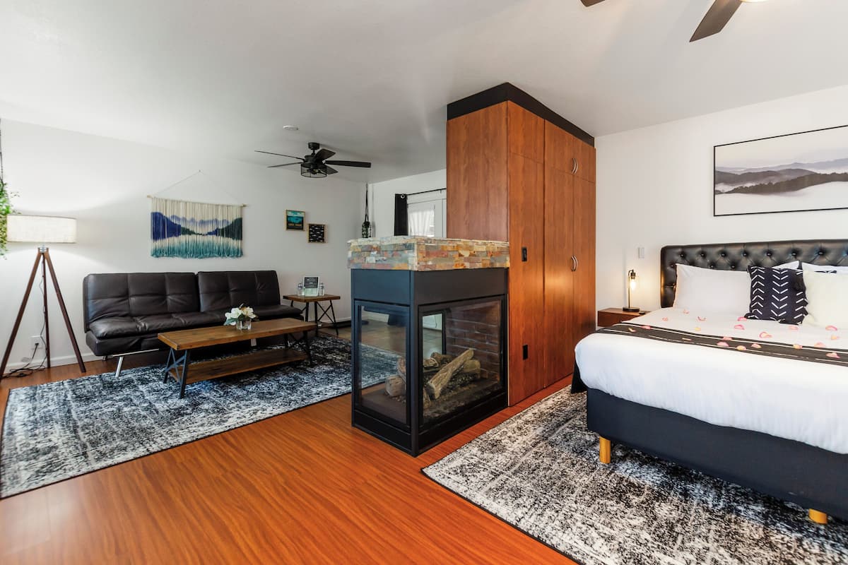 A modern bedroom with a bed, a sofa, a fireplace, and a ceiling fan.