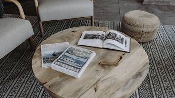 A round wooden coffee table with magazines and a book, surrounded by patterned rugs and a chair.
