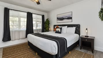 A bedroom with a bed, a nightstand, a ceiling fan, a window with curtains, and a wall-mounted picture.
