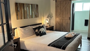 Un dormitorio con una cama, una mesita de noche, una lámpara de pared, un ventilador de techo y una puerta corredera que da a un balcón.