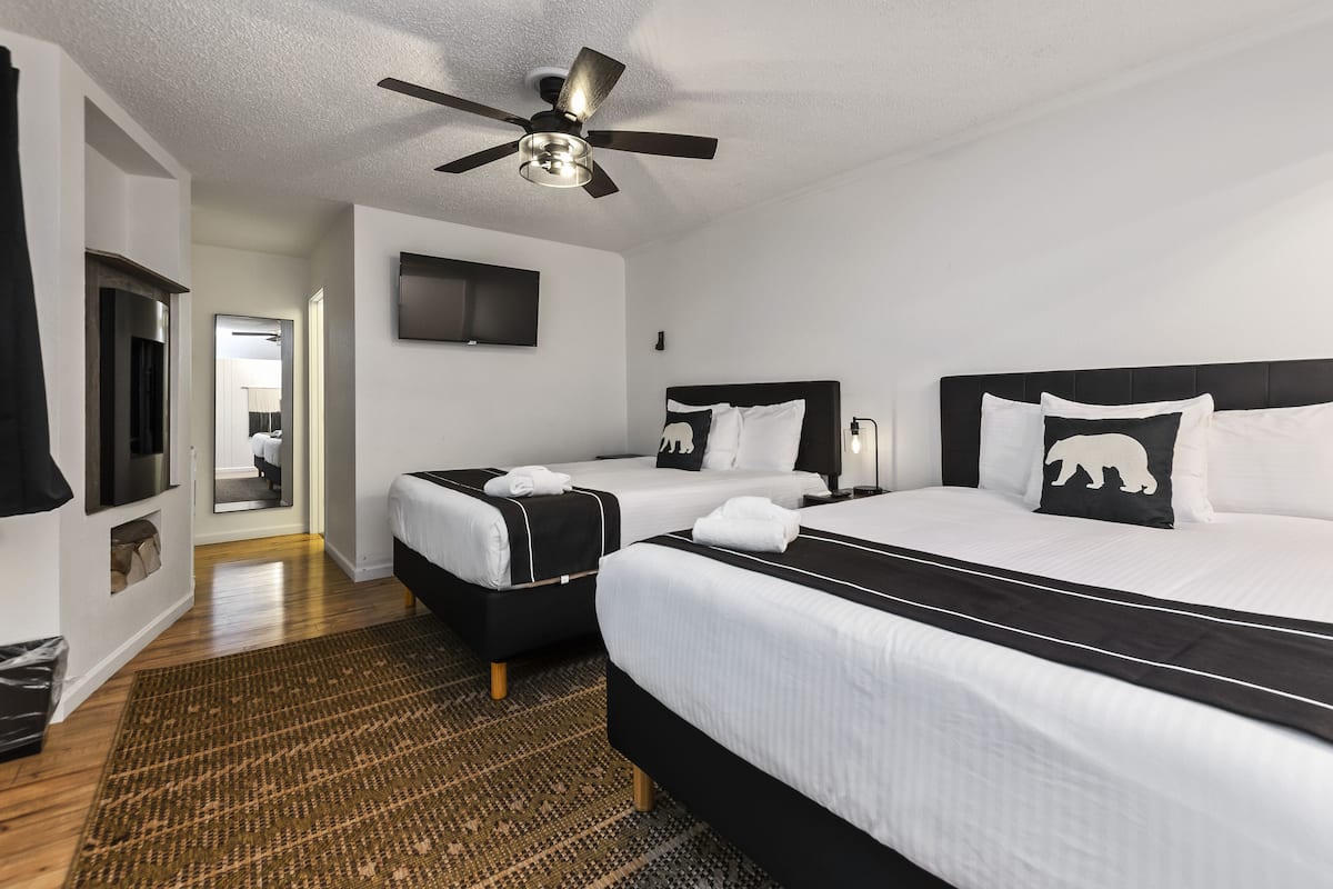 A hotel room with two beds, a ceiling fan, a TV, and a patterned rug.