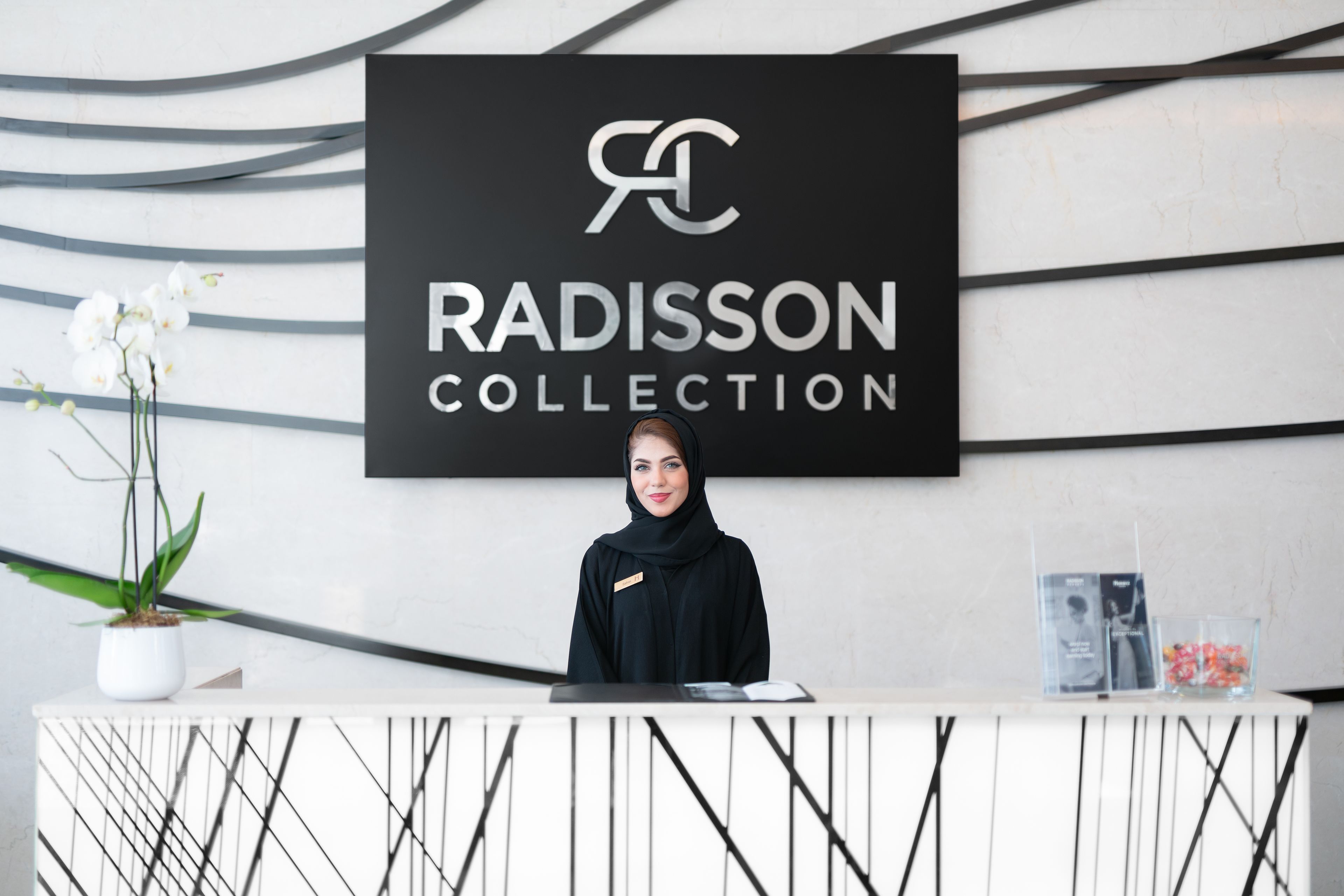 Una mesa de recepción con un letrero que dice "RADISSON COLLECTION" y una orquídea en maceta.