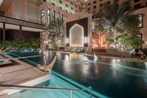 An indoor swimming pool with a glass ceiling, palm trees, and lounge chairs.