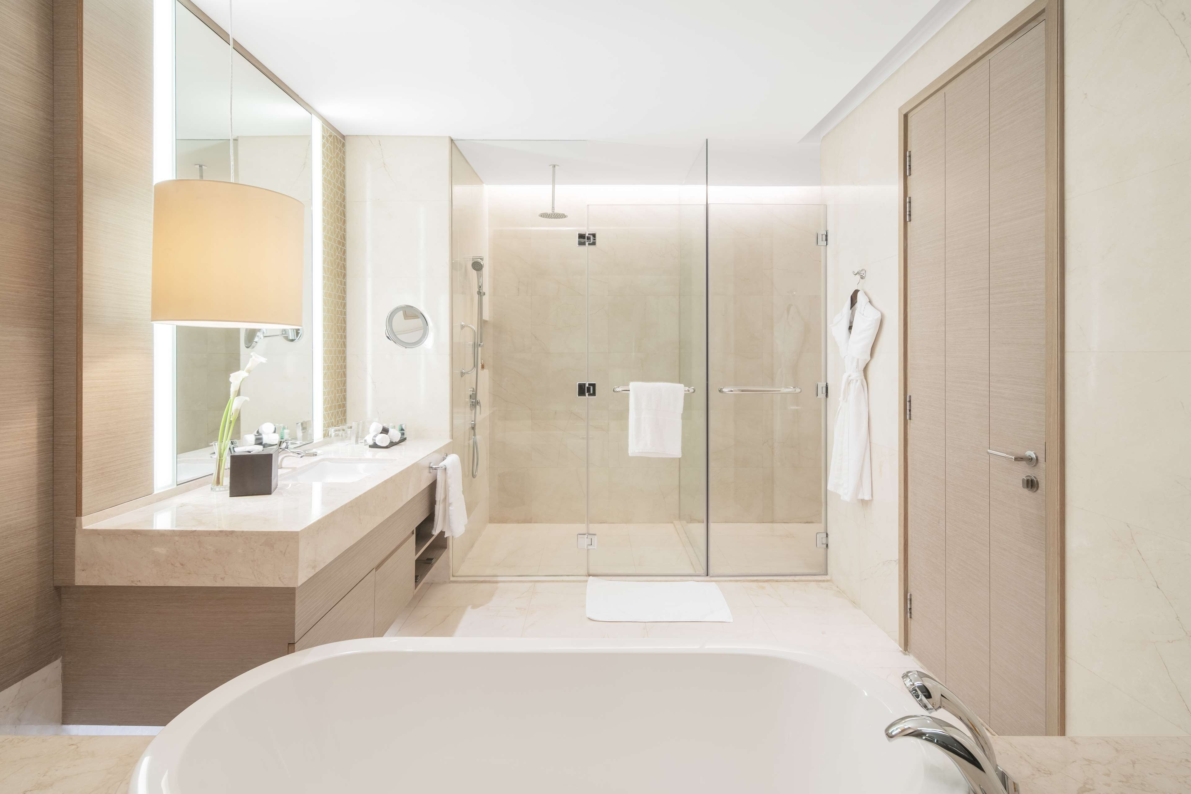 A modern bathroom with a large bathtub, a glass-enclosed shower, and a vanity with a mirror and towel rack.