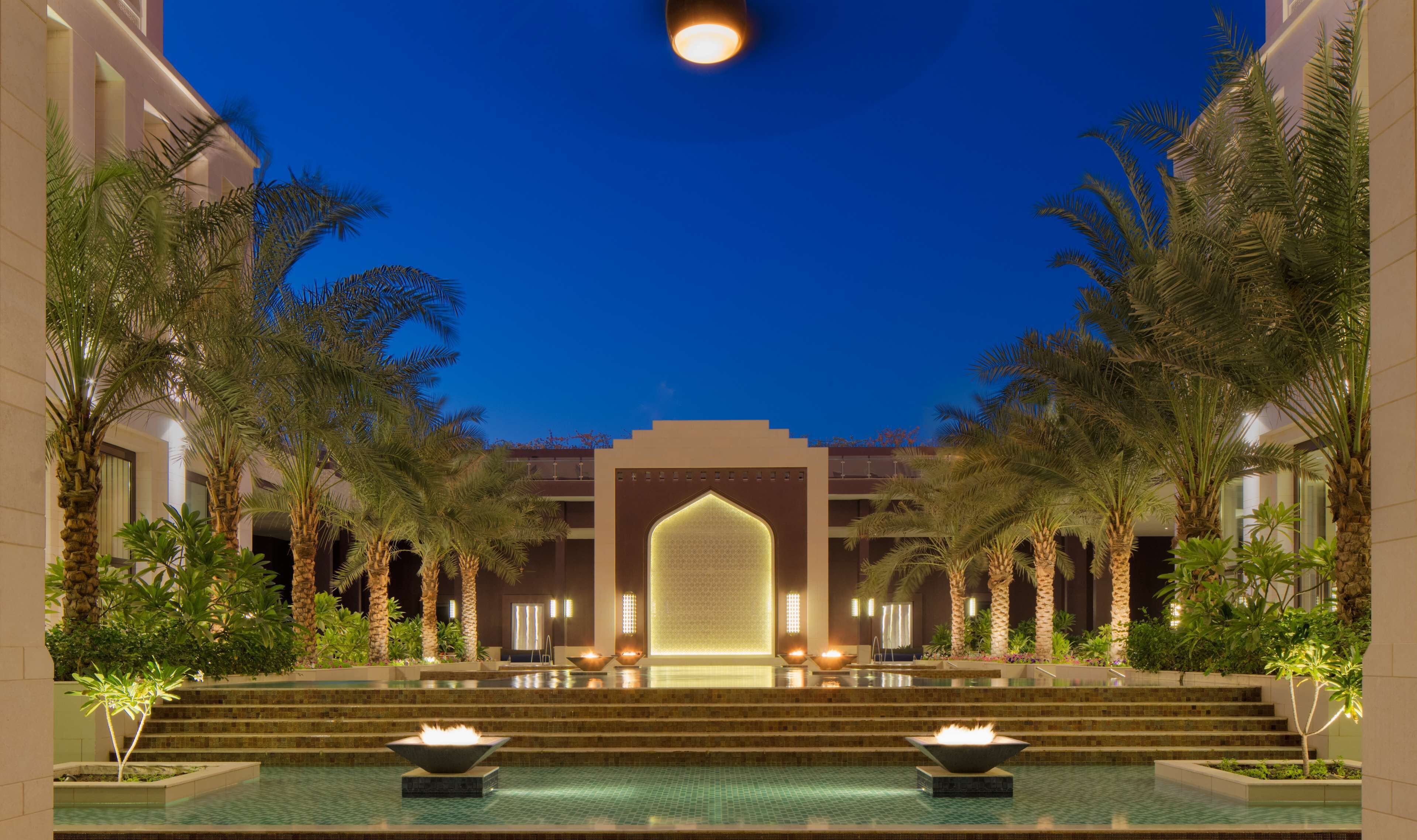 A pool area with a central fountain, palm trees, and a building with a large entrance.