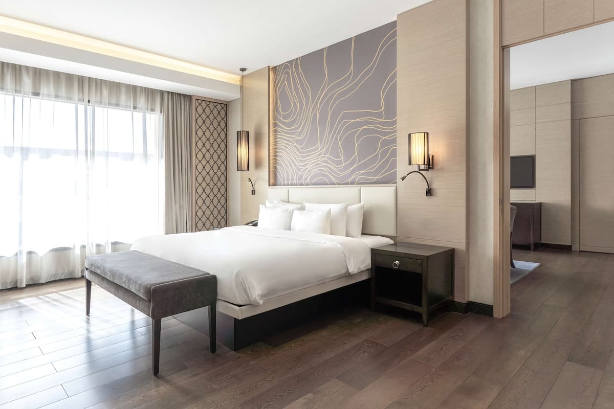 A modern hotel room with a large bed, bedside tables, a bench, and a TV.
