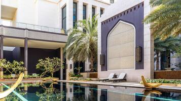 A modern indoor pool area with clear water, lounge chairs, palm trees, and a decorative wall with intricate patterns.