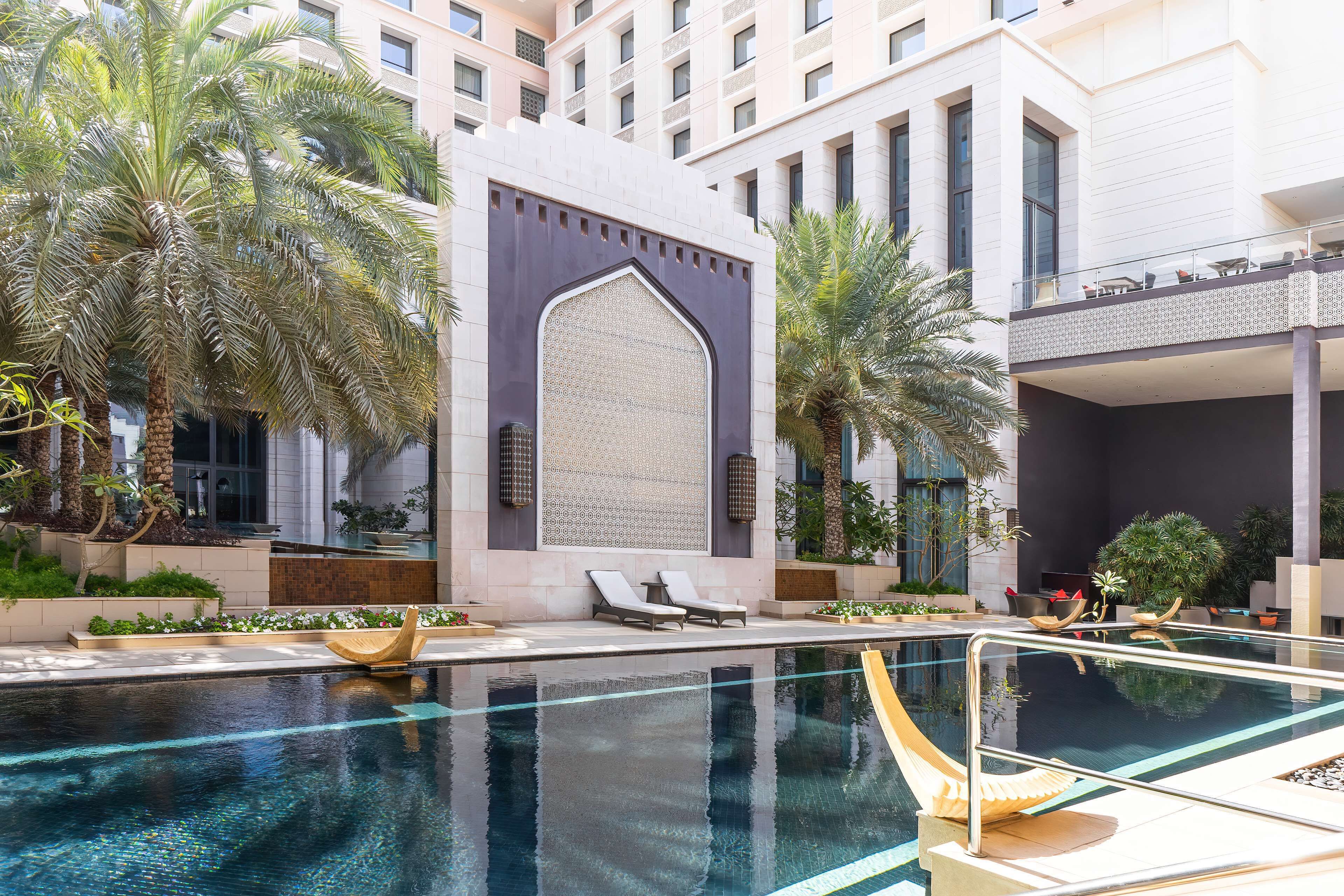 A modern hotel pool area with a clear pool, lounge chairs, and palm trees.