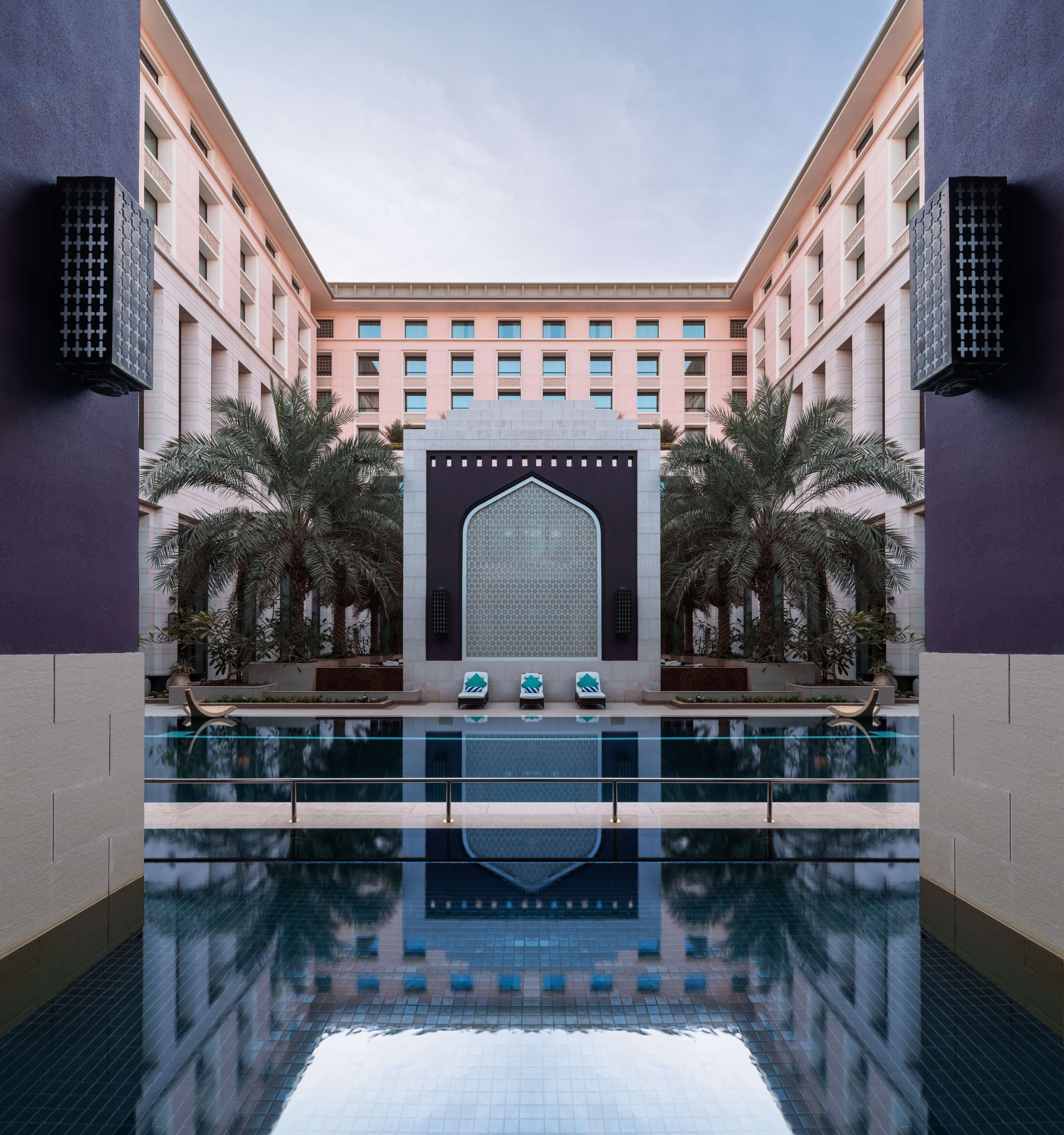 Un moderno vestíbulo de hotel con una piscina central, palmeras y un muro con diseño.