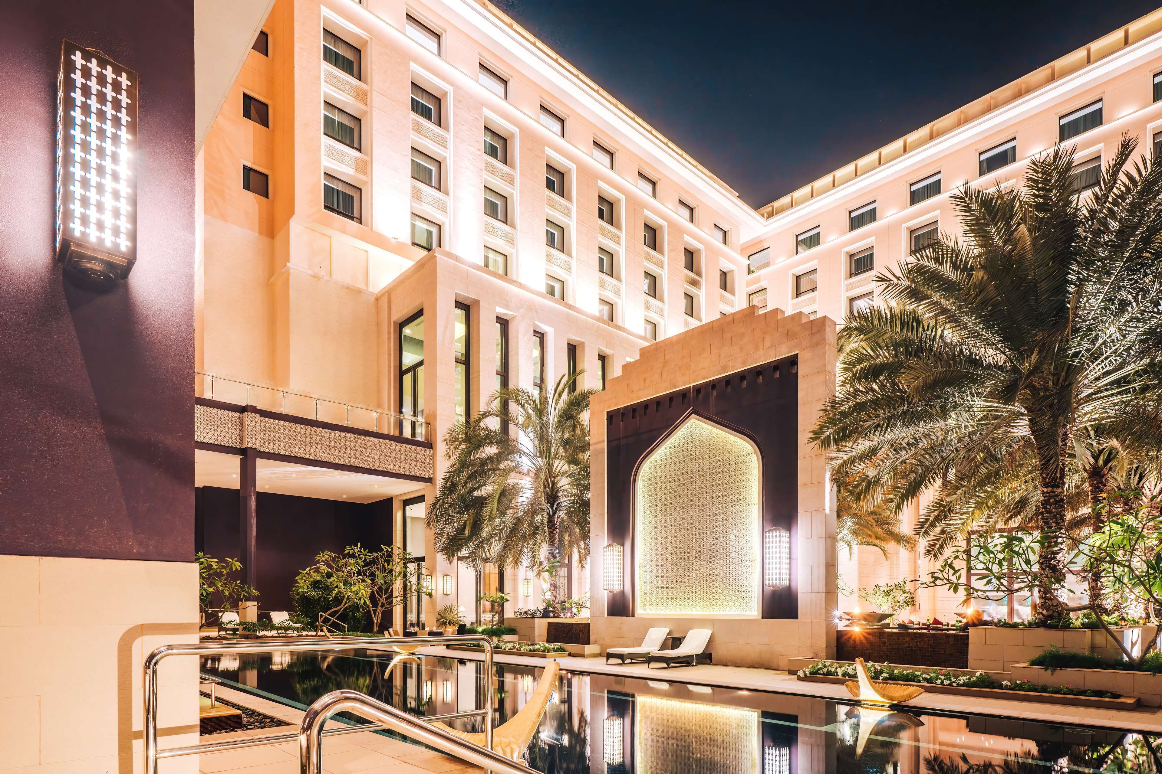 Un vestíbulo de hotel con piscina, palmeras y una gran pared iluminada.