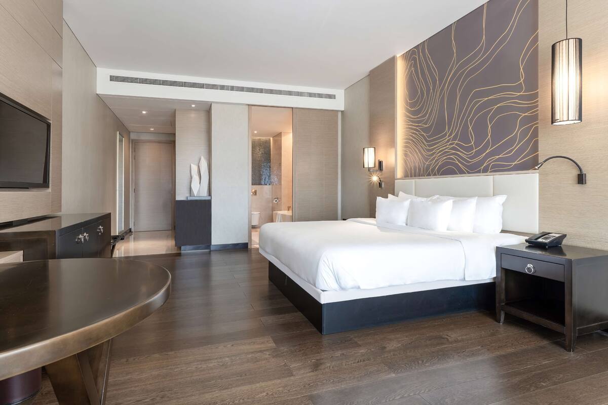 A modern hotel room with a large bed, bedside table, and a flat-screen TV.