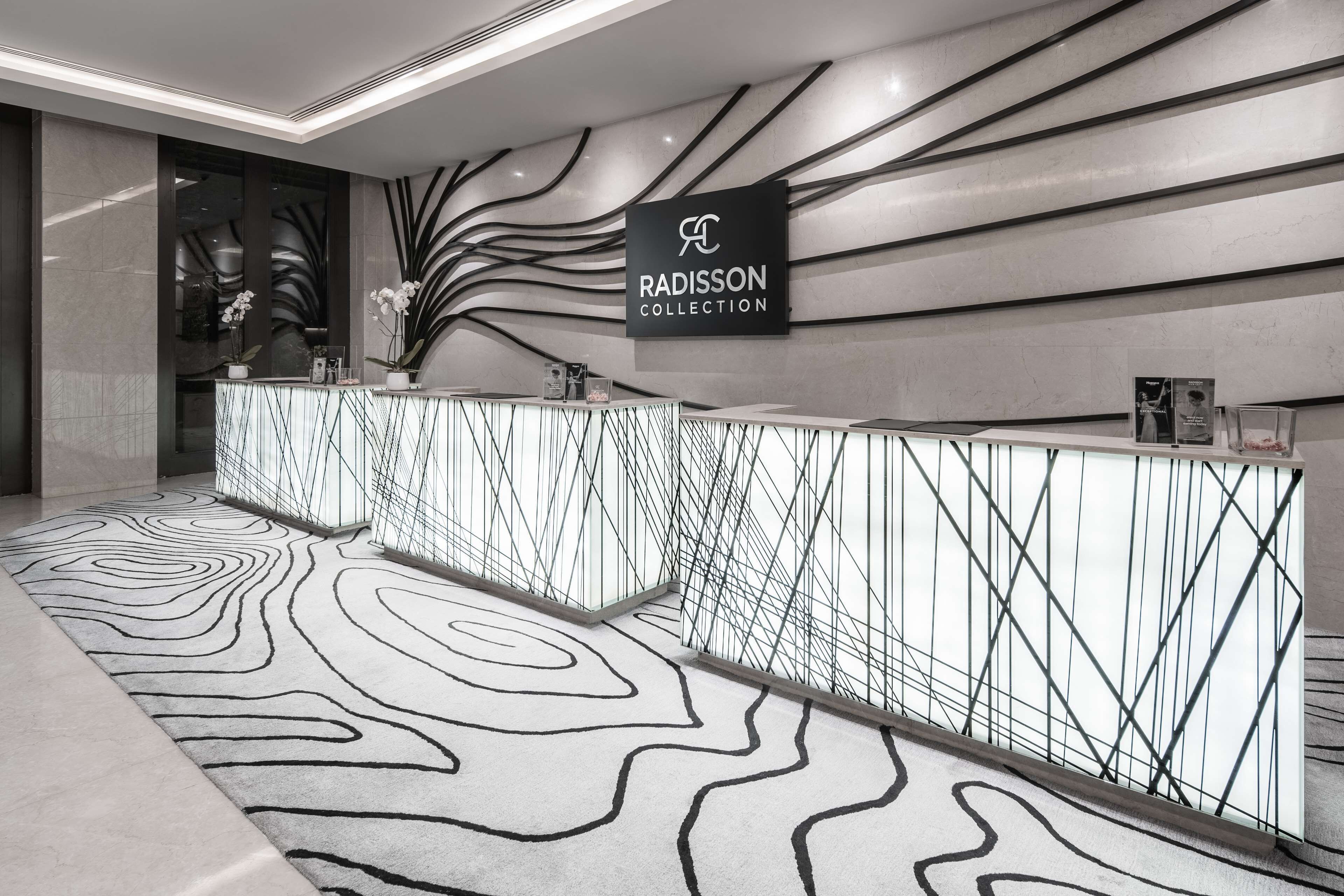 Ein Empfangsbereich im modernen Stil mit einem Marmor-Empfangsschalter, einem Schild mit der Aufschrift 'Radisson Collection' und einem gemusterten Teppich.