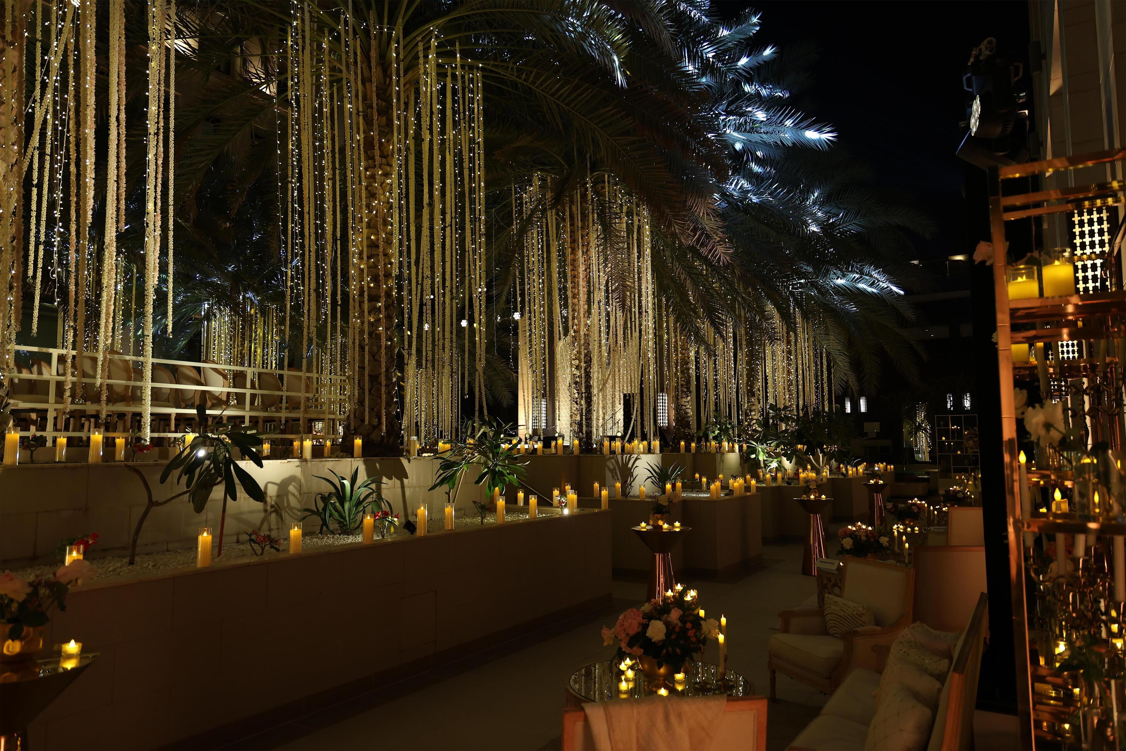 A luxurious indoor setting with a long corridor lined with tall, illuminated columns and a series of tables and chairs arranged along the sides.