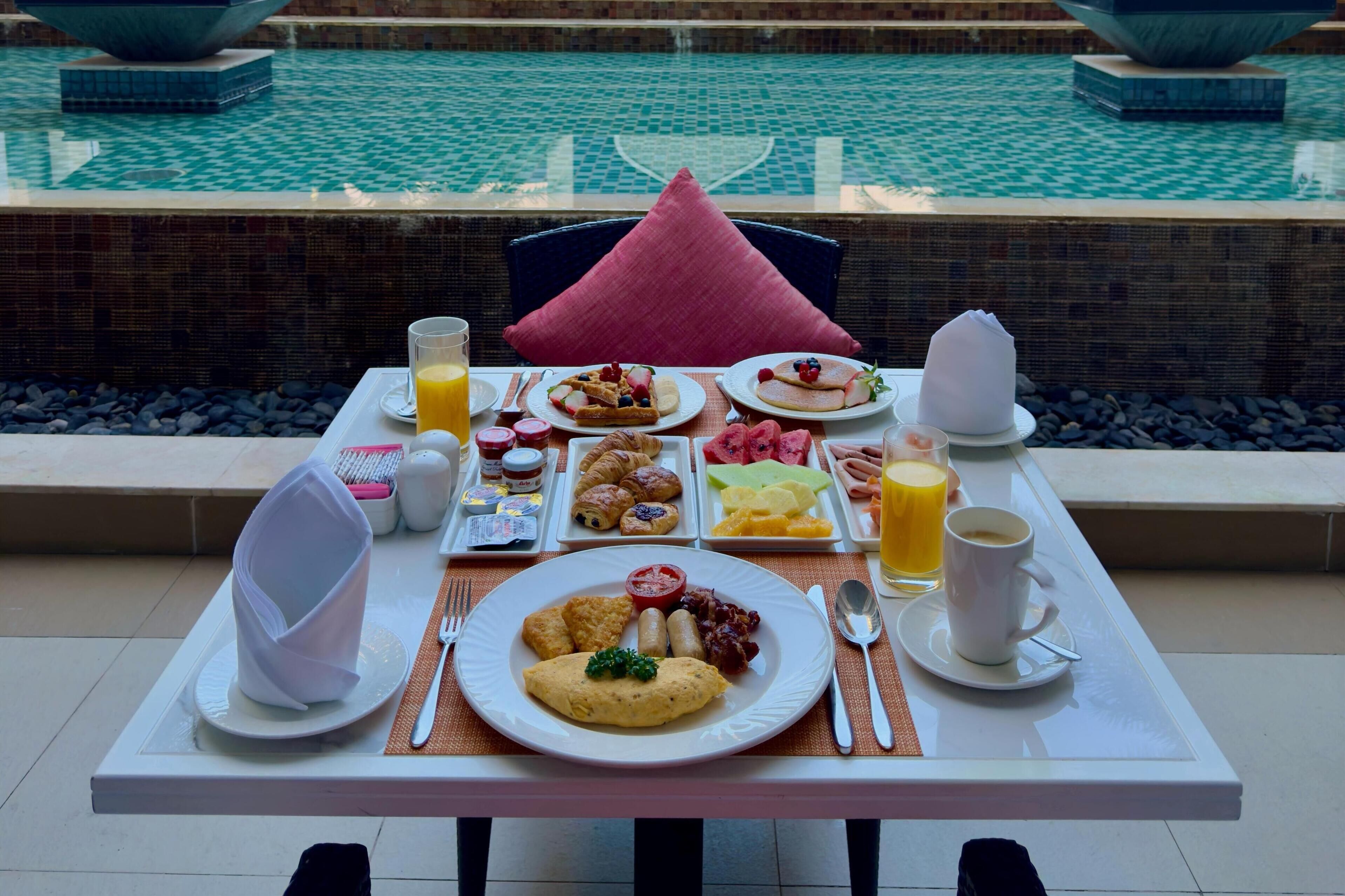Une table de petit-déjeuner avec divers plats, une tasse de café et une vue sur une piscine.