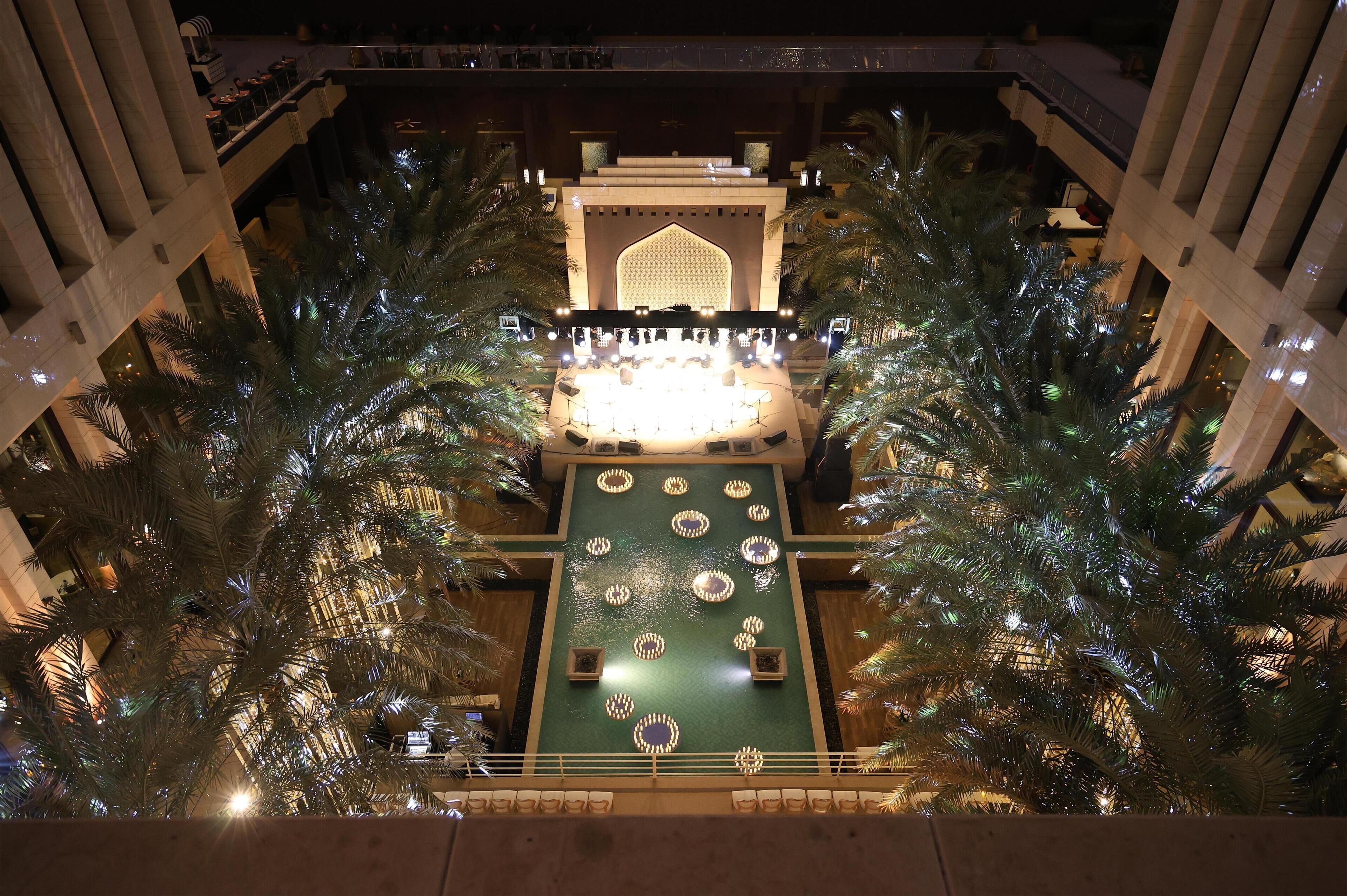 An indoor atrium with a central stage, palm trees, and a patterned ceiling.