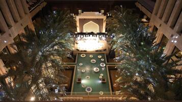 An indoor atrium with a central stage, palm trees, and a patterned ceiling.