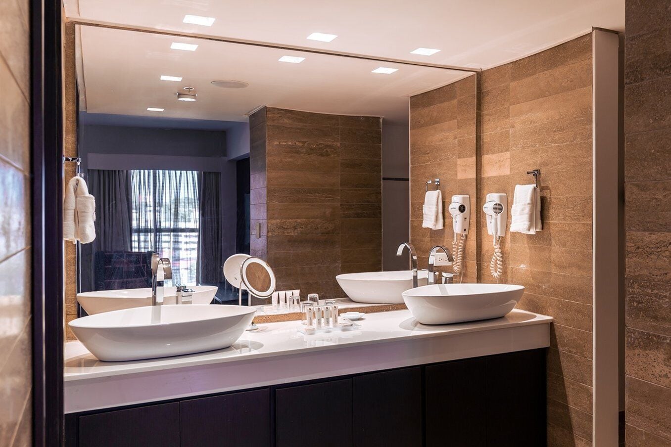 A modern bathroom with two large white sinks, a mirror, and a vanity with toiletries.