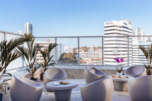 Eine Dachterrasse mit moderner Sitzgelegenheit, Topfpflanzen und Blick auf Stadtgebäude.