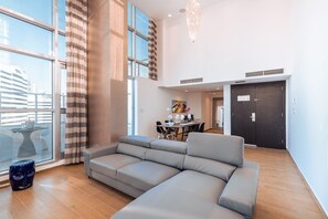 Ein modernes Wohnzimmer mit einer großen Eckcouch, einem Essbereich mit Tisch und Stühlen sowie einem Blick auf die Stadt durch große Fenster.