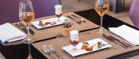 Una mesa de comedor dispuesta con platos, cubiertos y copas de vino.