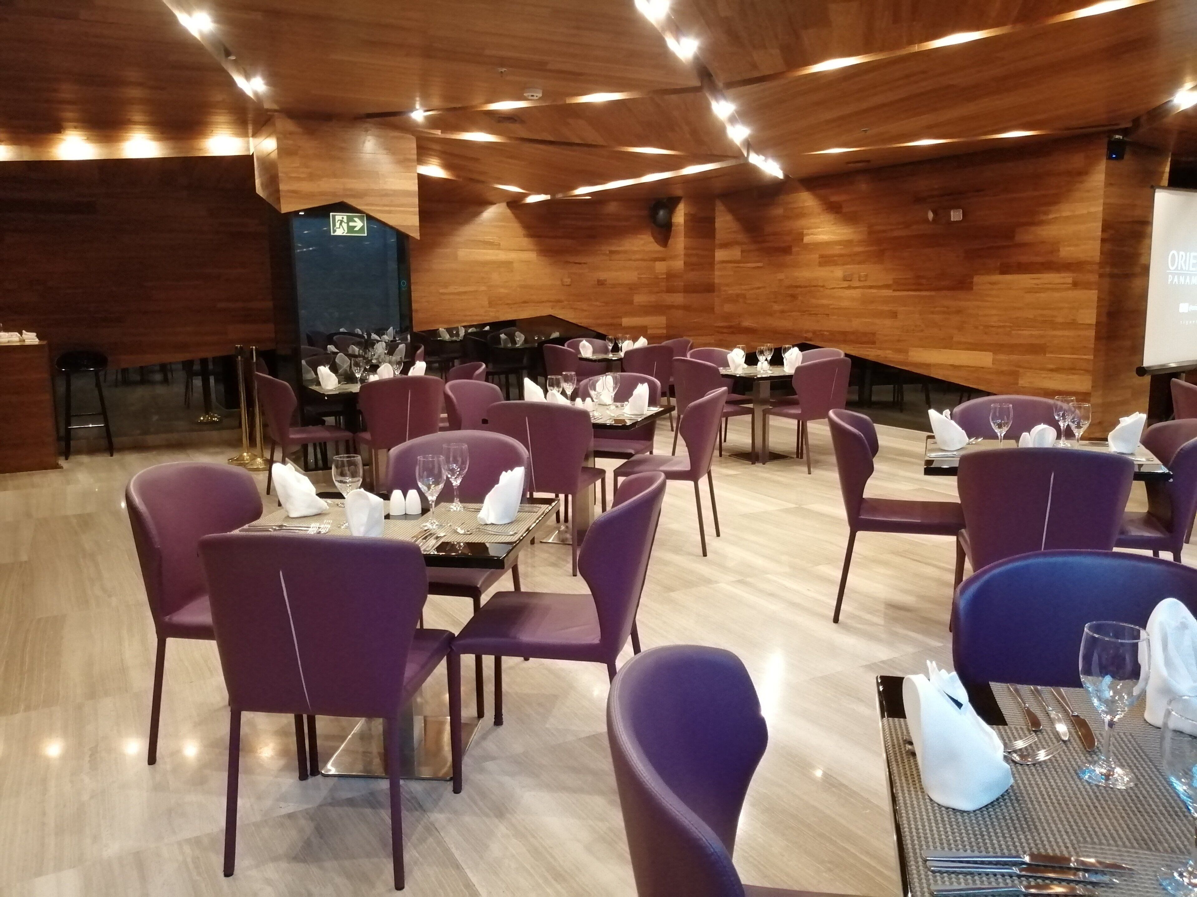 Ein Restaurant mit violetten Stühlen und Tischen, einer Holzbalkendecke und einer Projektionsleinwand im Hintergrund.