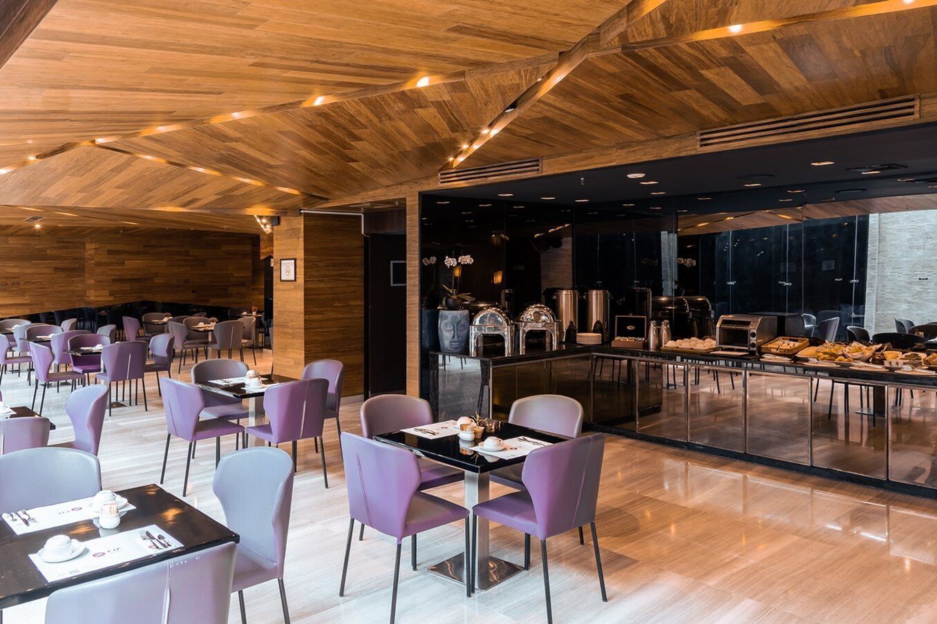 Un restaurante moderno con paneles de techo de madera, sillas moradas y una zona de bufé con diversas opciones de comida.