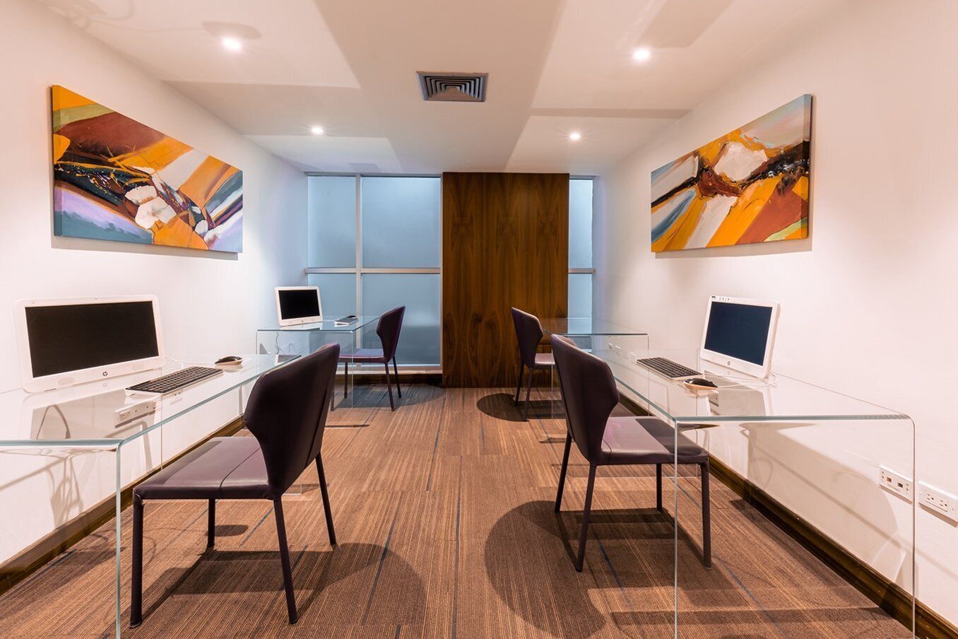 A modern office with glass desks, two computers, and chairs.