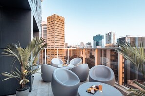 Eine Dachterrasse mit moderner Sitzgelegenheit, einem kleinen Tisch mit Snacks und Blick auf die Skyline der Stadt.