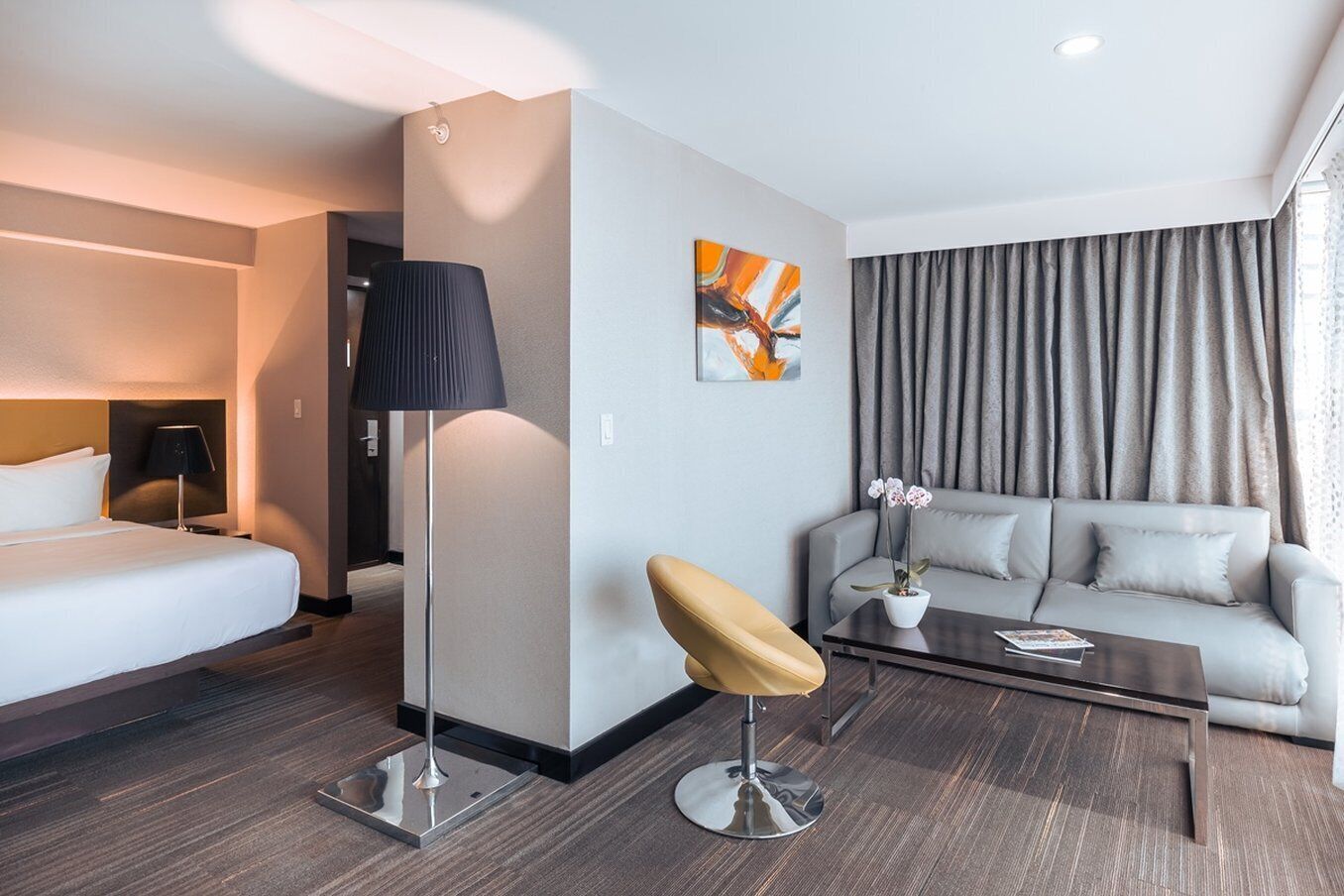 A hotel room with a bed, a desk, a chair, a sofa, and a coffee table.
