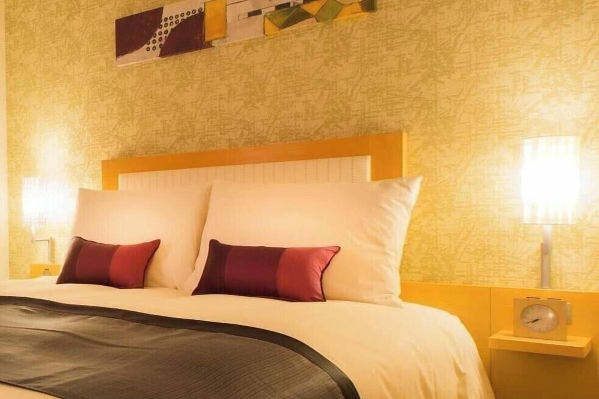 A hotel room with a large bed, two bedside tables with lamps, a wall clock, and a decorative piece above the bed.