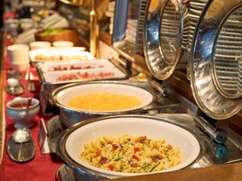 Un bufé con platos de pasta, incluyendo un recipiente grande de pasta con tomates y hierbas.
