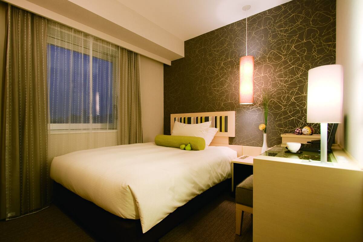 A hotel room with a bed, a desk, a lamp, and a decorative wall.
