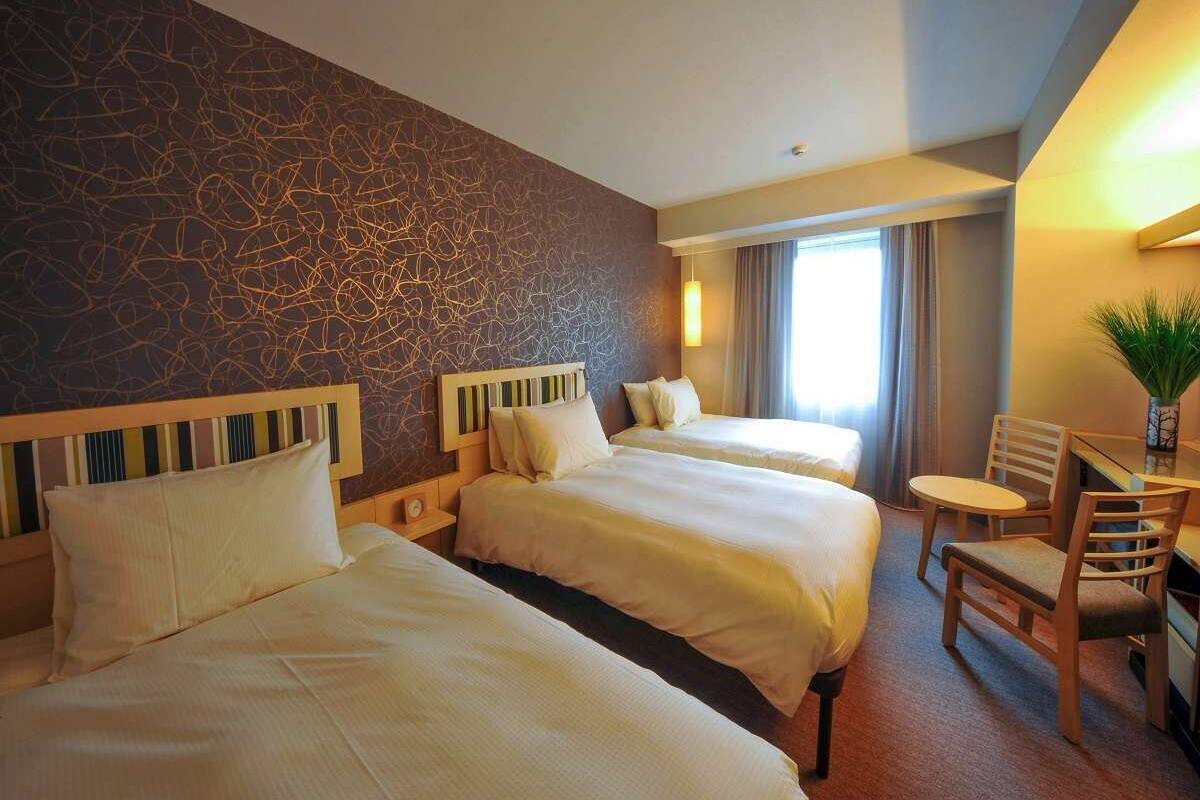 A hotel room with two beds, a desk, and a chair.