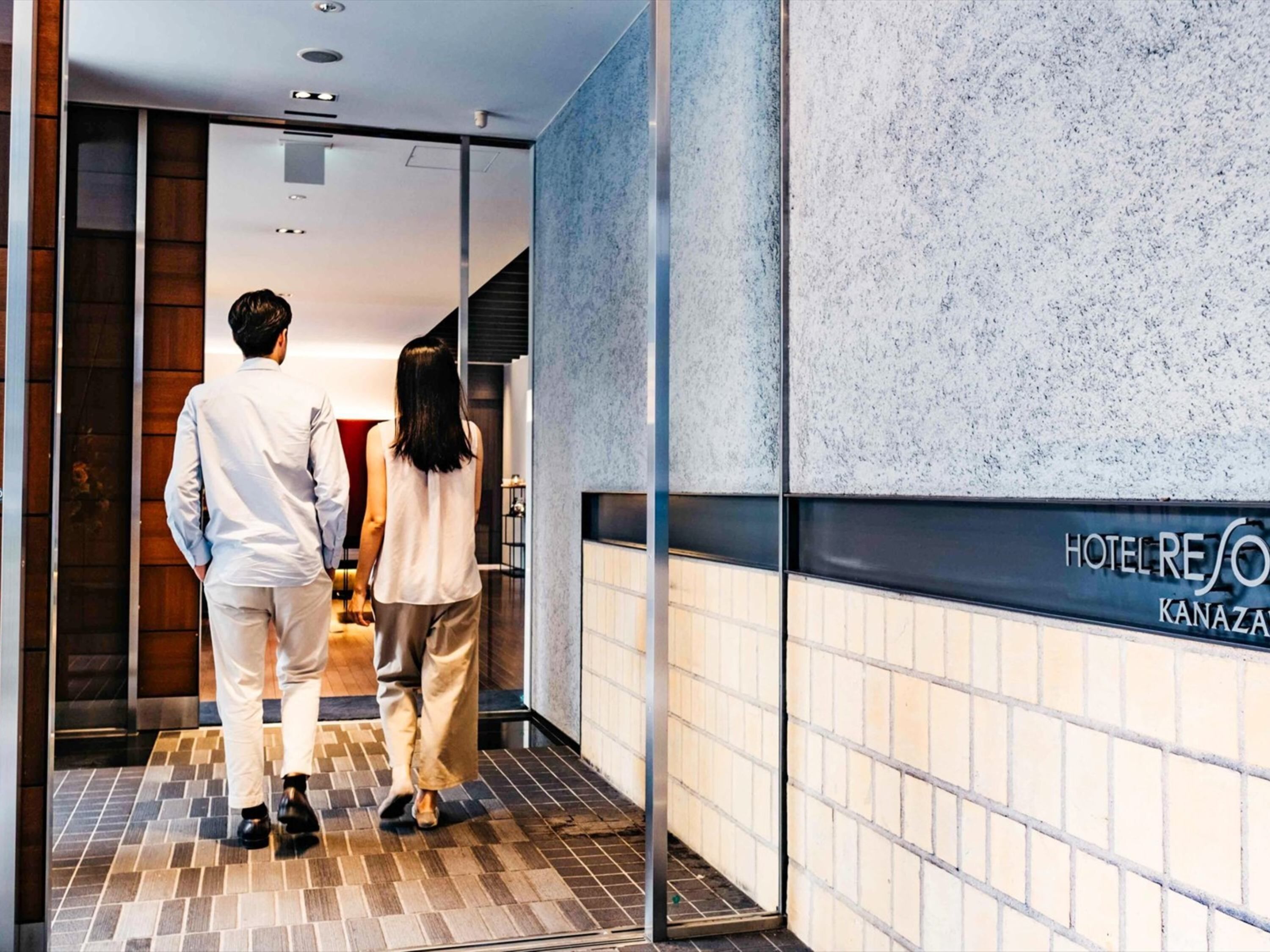 L'entrée d'un hôtel au design moderne, avec un sol carrelé et une enseigne indiquant « HÔTEL RESO KANAZAWA ».