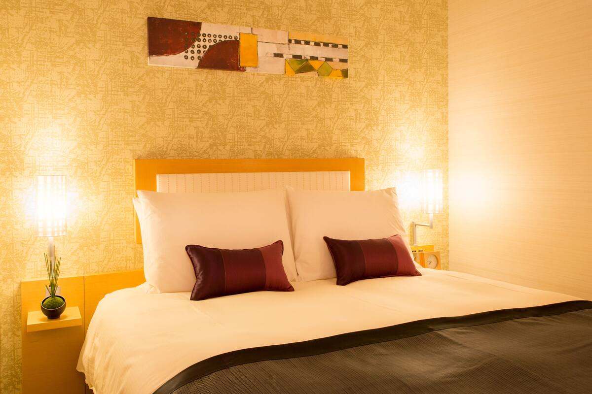 A neatly made bed with a headboard, two bedside lamps, and a small plant on the nightstand.