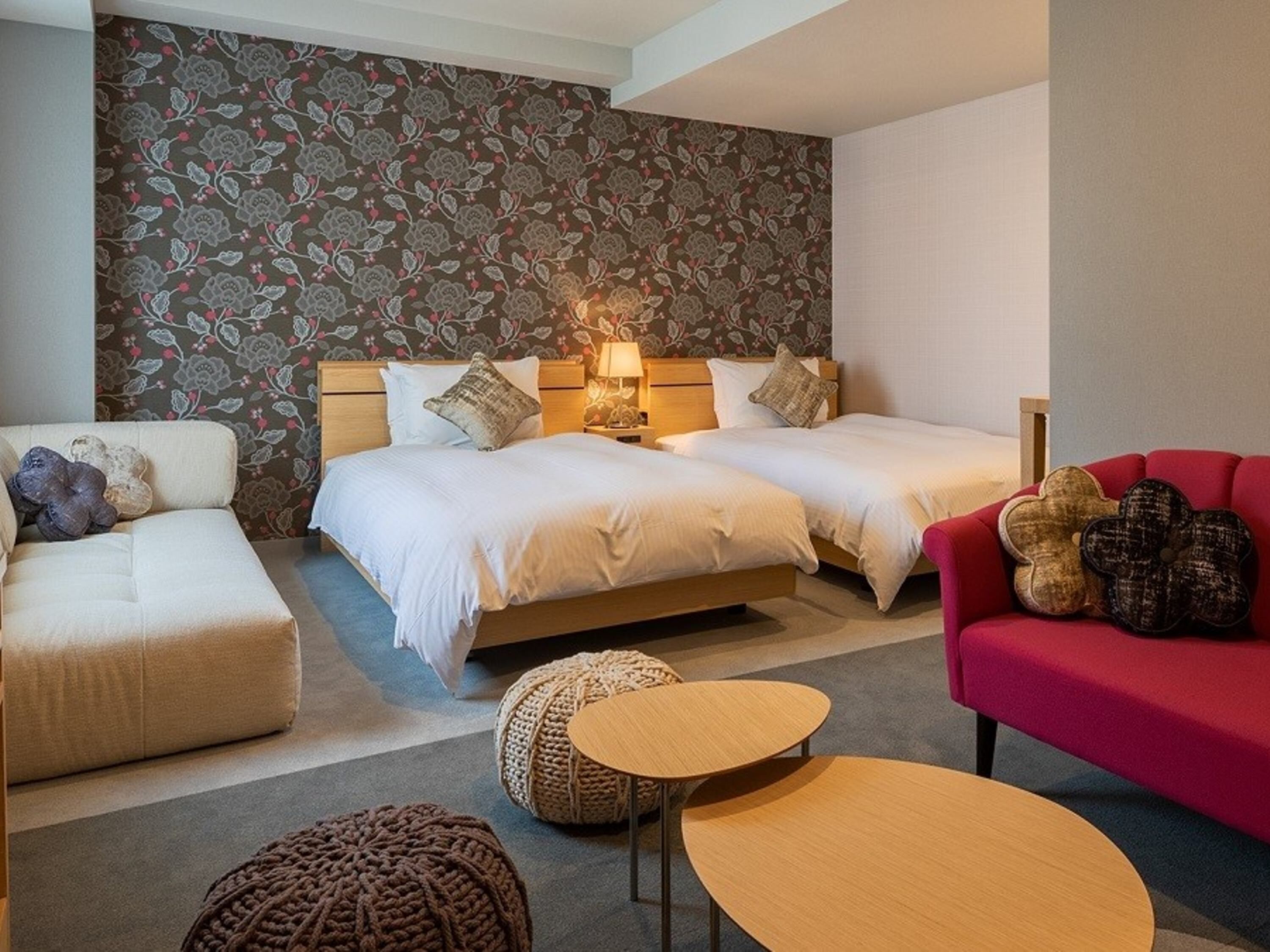 A hotel room with two beds, a red sofa, a beige sofa, and a small wooden table.