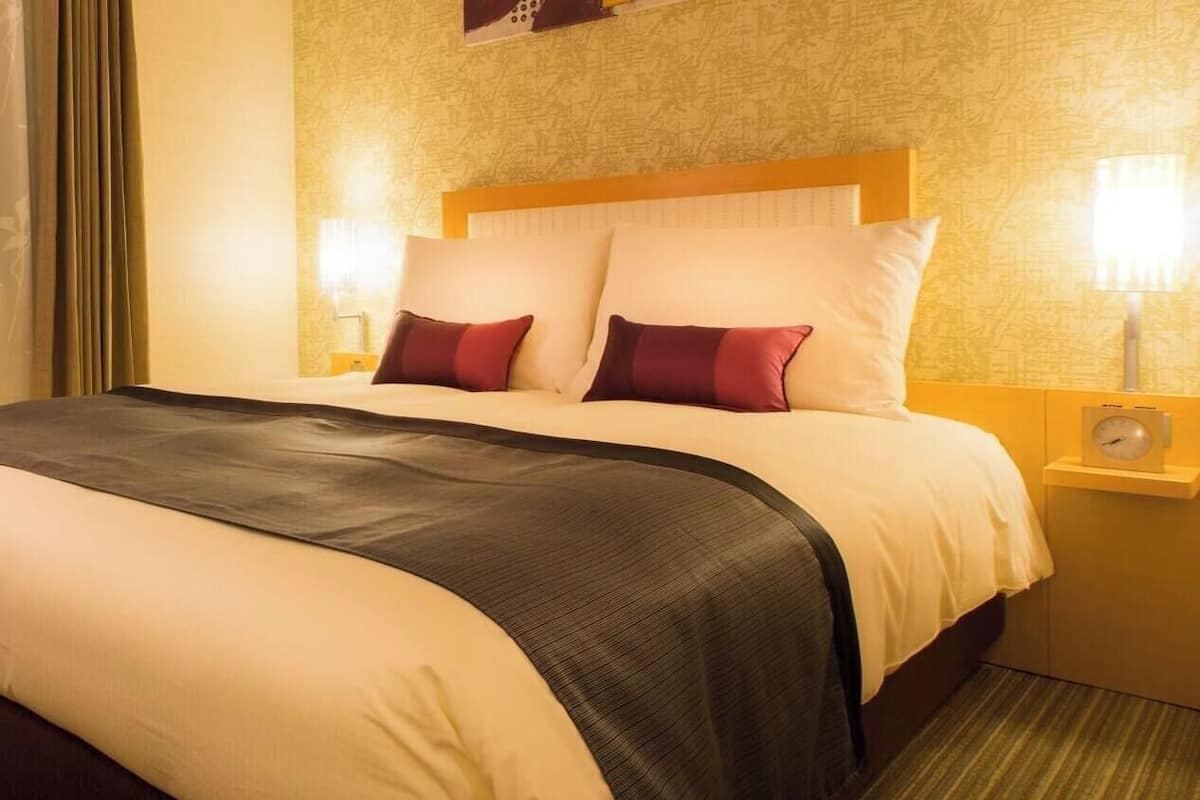 A hotel room with a bed, two bedside lamps, a clock, and a patterned wall.