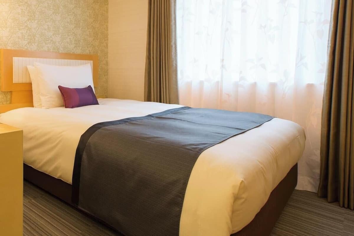 A hotel room with a large bed, a wooden headboard, a nightstand, and a window with curtains.