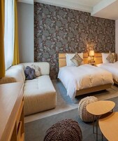 Una habitación con dos camas, un sofá rojo y una pequeña mesa. La habitación tiene papel tapiz floral y un cabecero de madera.
