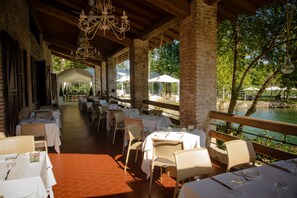 Un área de comedor al aire libre con mesas y sillas, un muro de ladrillo y vistas a un cuerpo de agua.