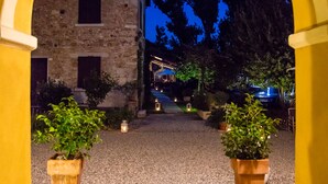 Une entrée en arc donnant sur un bâtiment, avec une cour recouverte de gravier et des plantes en pot.