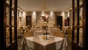 Un restaurant aux murs de pierre, aux portes en bois et aux tables dressées pour le repas.