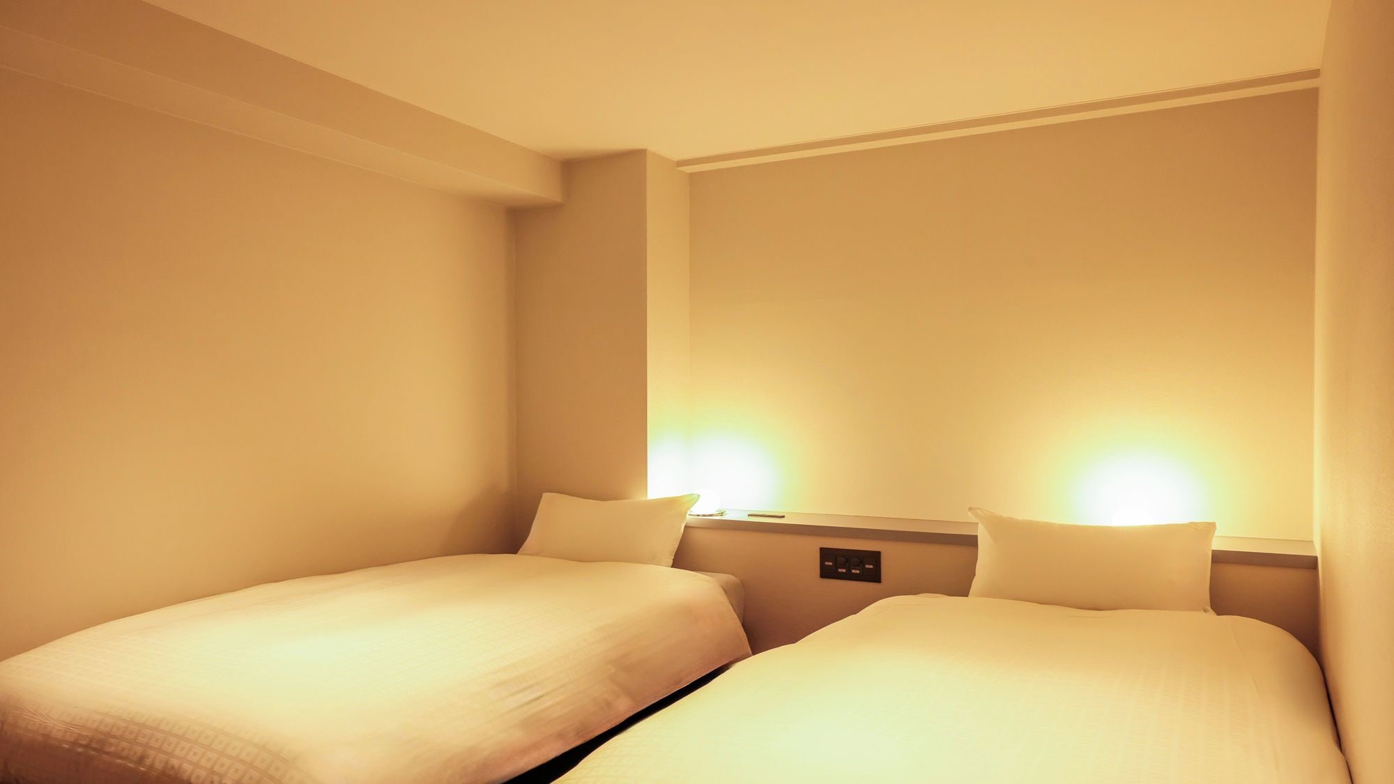 Une chambre d’hôtel avec deux lits simples, une table de chevet avec une lampe et un panneau de commande fixé au mur.