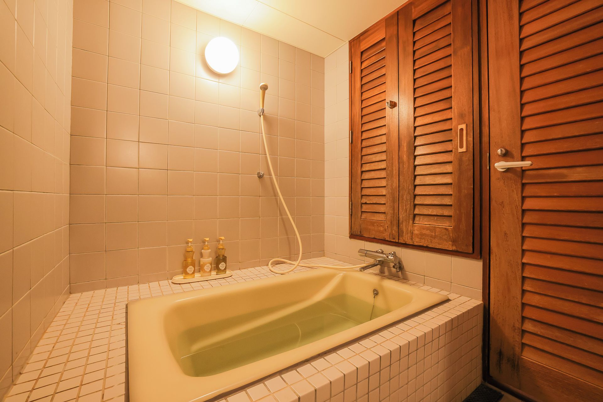 A bathroom with a bathtub, a shower, and wooden shutters on the door.