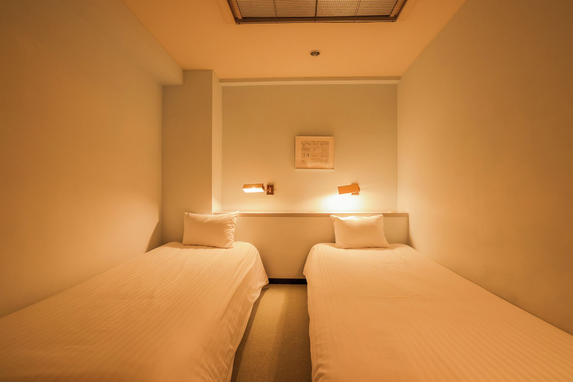 A room with two single beds, a small table, and a wall-mounted light fixture.