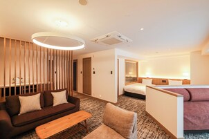Habitación de hotel con sofá, una mesita, una silla, una cama y una zona de descanso separada.